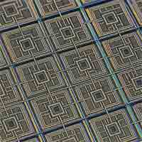 Macro photograph of microchips showing a precise grid pattern with dark gray polysilicon gate structures and colorful grid-like lines reflecting light.
