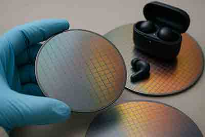 Gloved hand holding patterned silicon wafer with earbuds in background